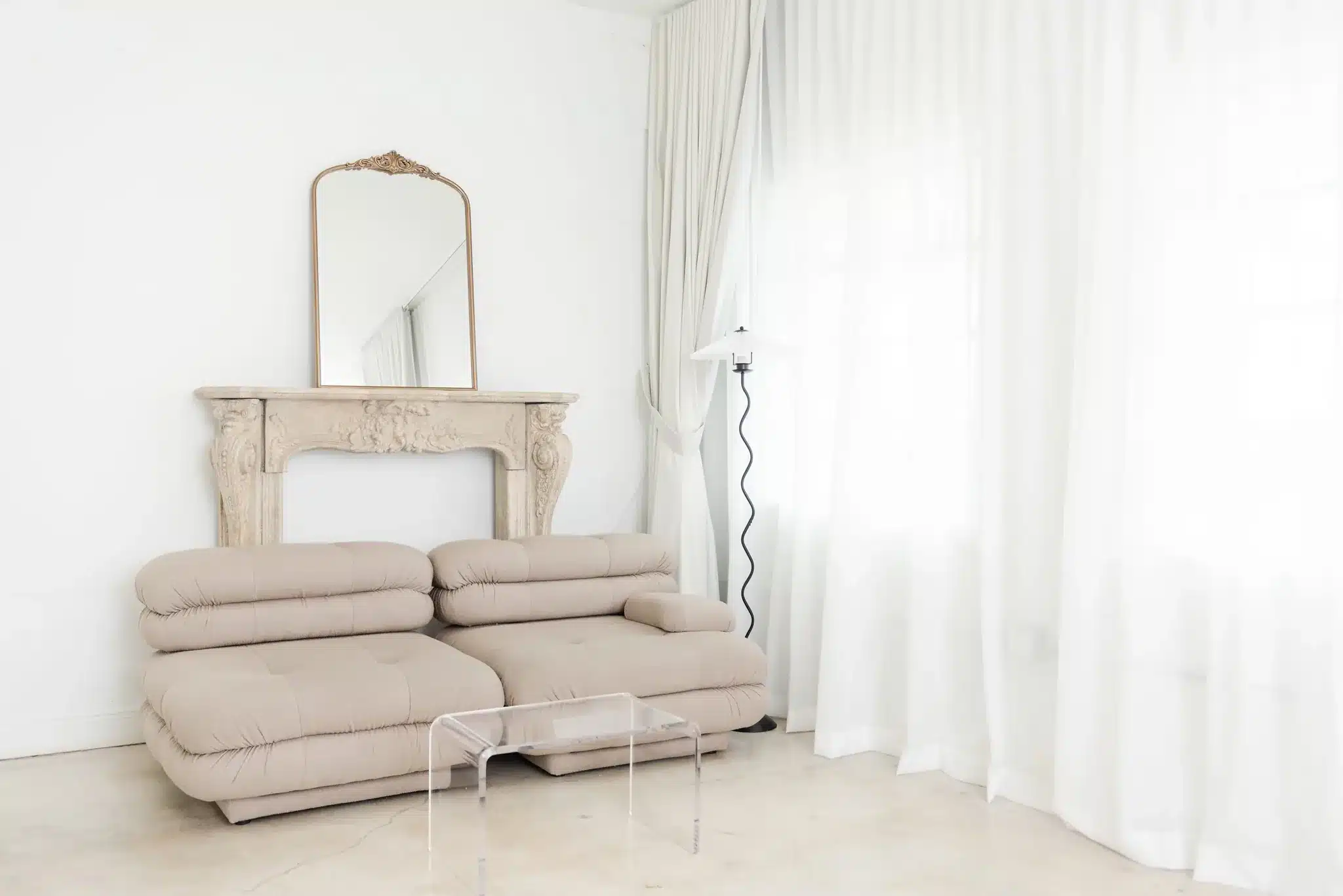 Lounge set with a beige tufted sofa, carved fireplace mantel and gold mirror in a Miami studio