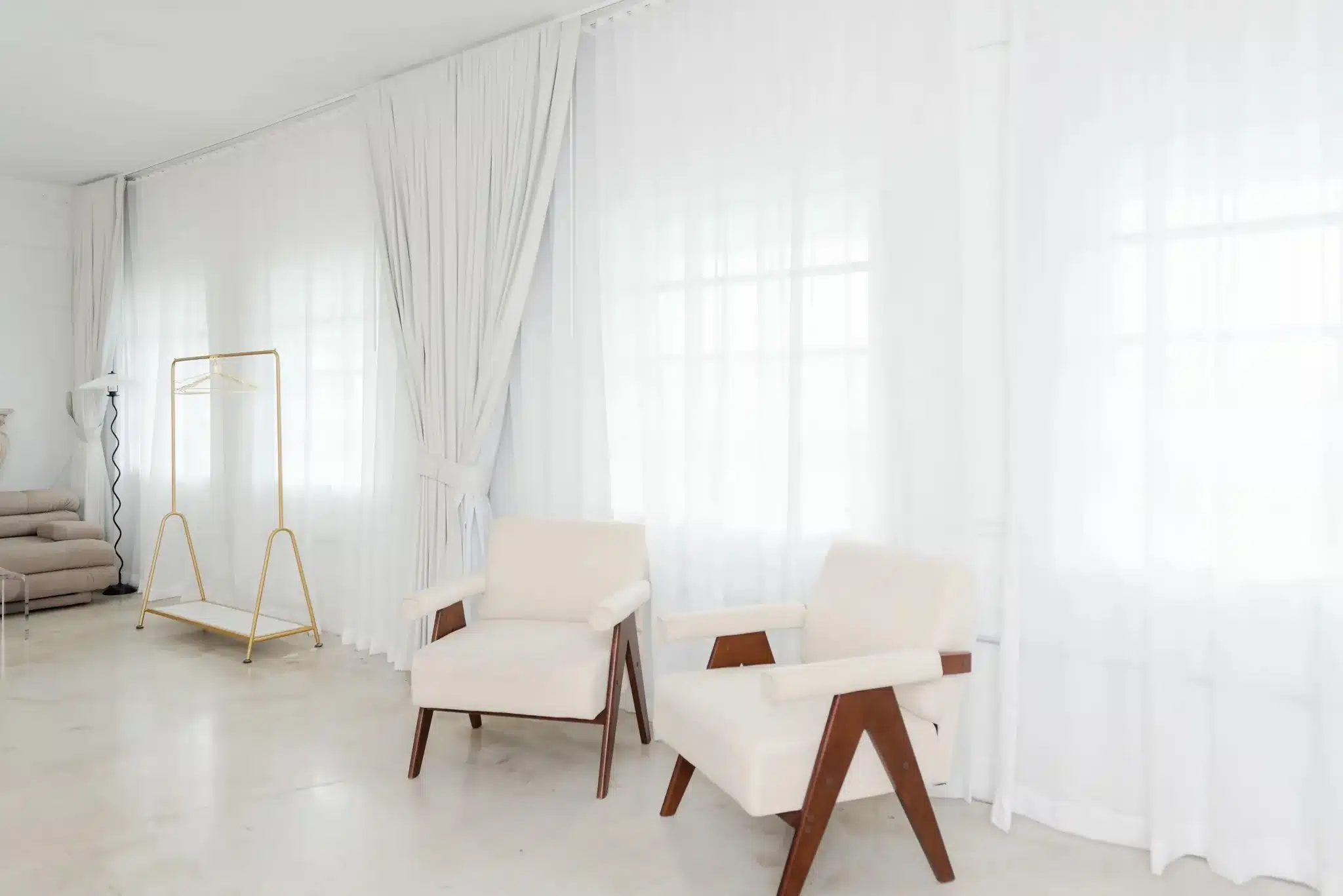 Two cream armchairs in front of sheer curtains in a natural-light Miami photo studio set
