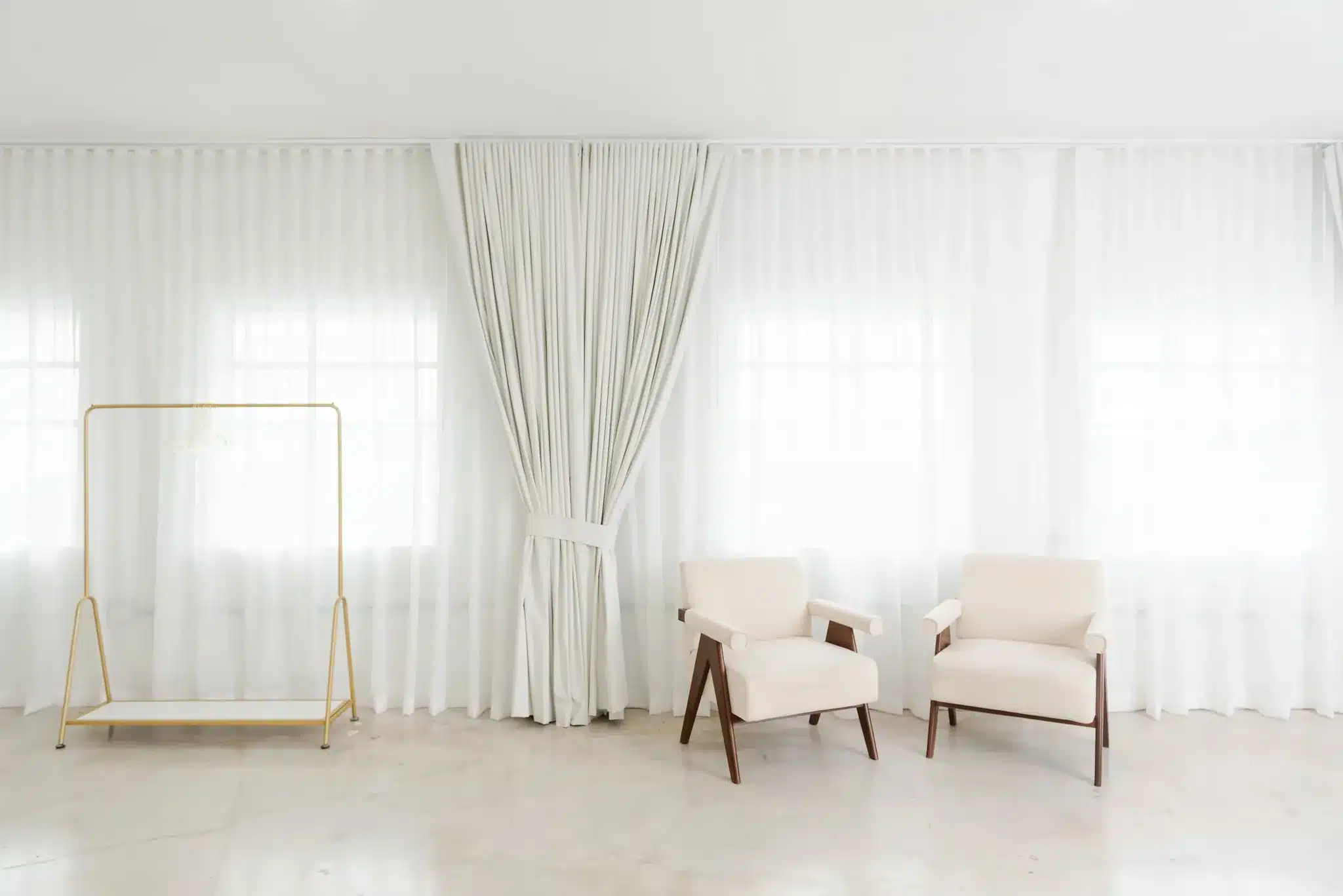 Cream wood-frame armchairs centered on a sheer curtain backdrop in a bright Miami studio