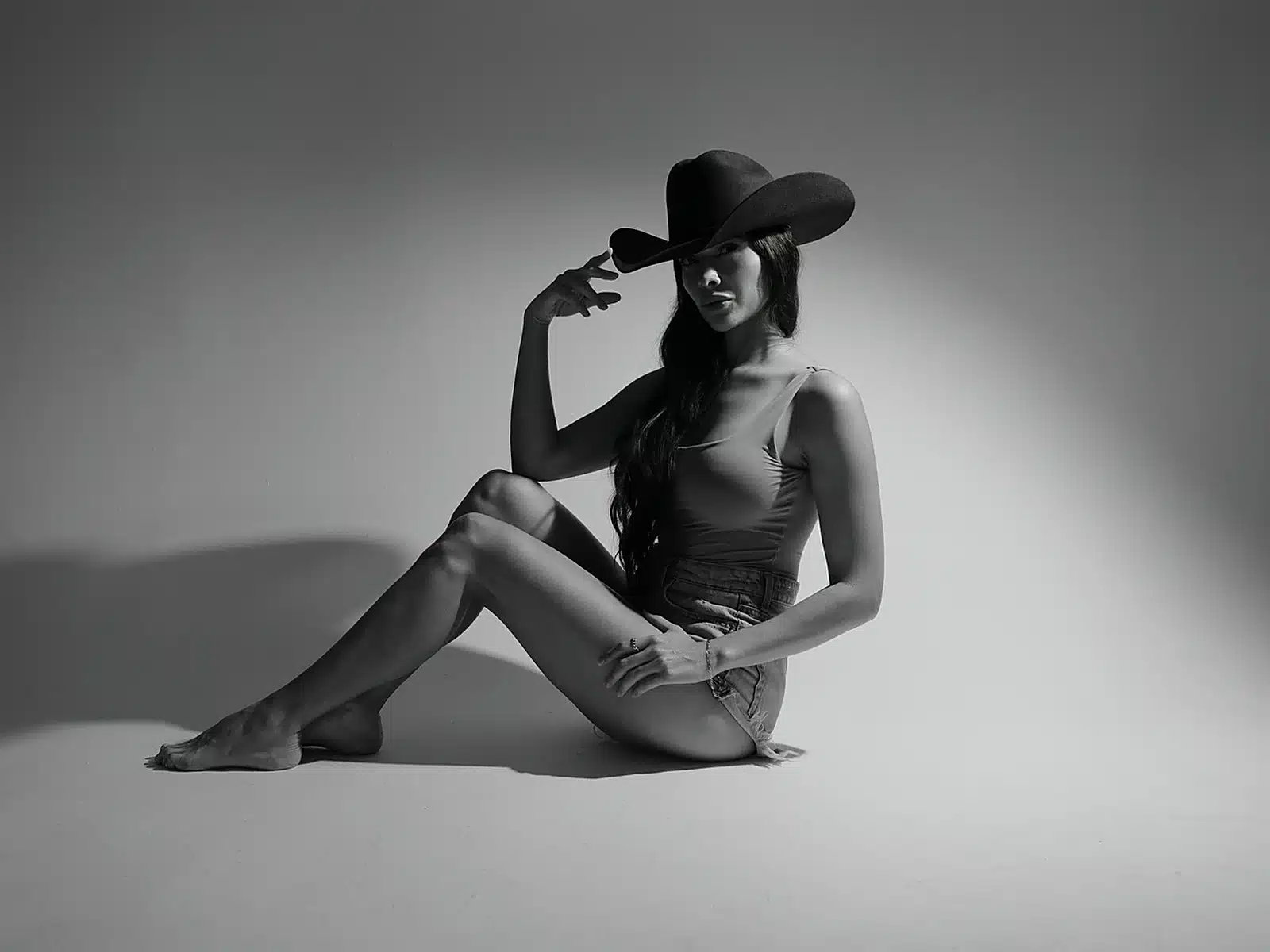 Black and white photo of a woman in a bodysuit and cowboy hat seated on the studio floor at a Miami photo studio