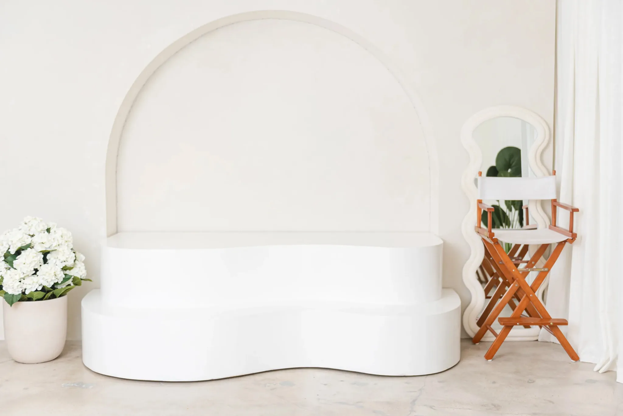 White sculptural arch riser platform styled with flowers and a wavy mirror at a Miami studio